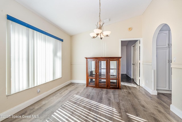 unfurnished dining area with baseboards, arched walkways, lofted ceiling, wood finished floors, and a notable chandelier