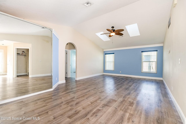 empty room with visible vents, arched walkways, baseboards, lofted ceiling with skylight, and wood finished floors