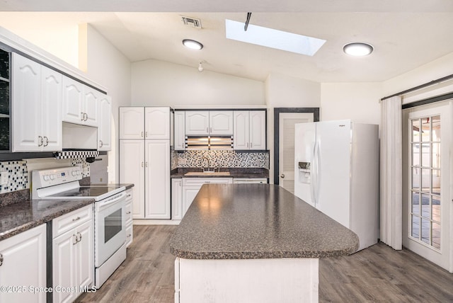 kitchen featuring lofted ceiling with skylight, dark countertops, white appliances, and a sink