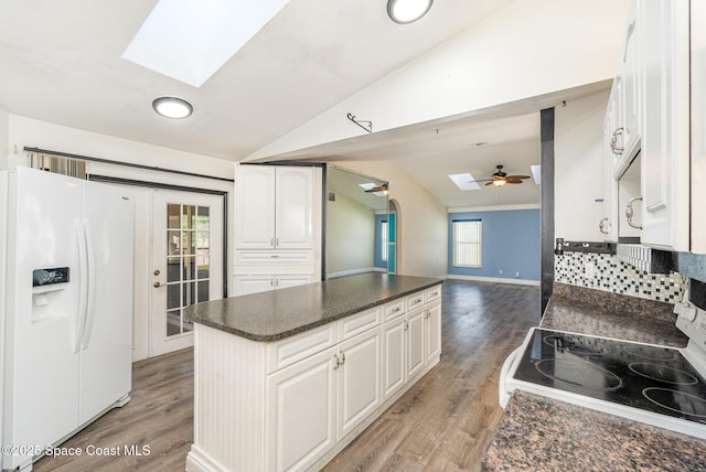 kitchen with vaulted ceiling with skylight, white appliances, white cabinetry, and light wood finished floors