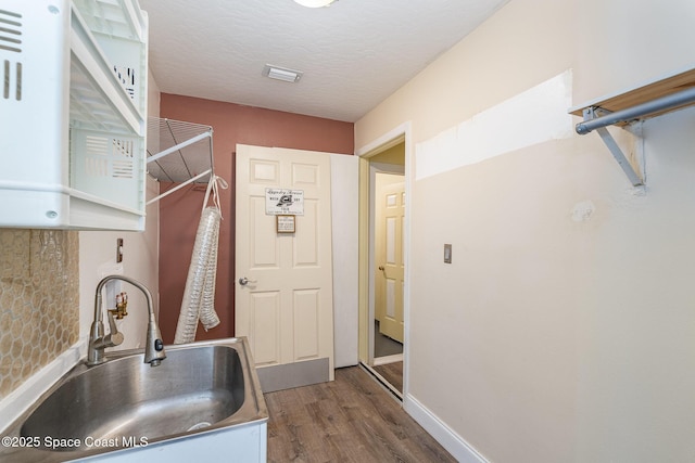 kitchen featuring a textured ceiling, wood finished floors, a sink, baseboards, and stainless steel counters