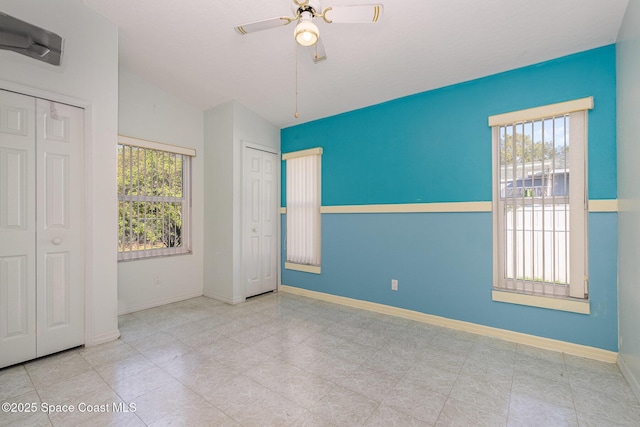 unfurnished bedroom with lofted ceiling, multiple windows, baseboards, and two closets