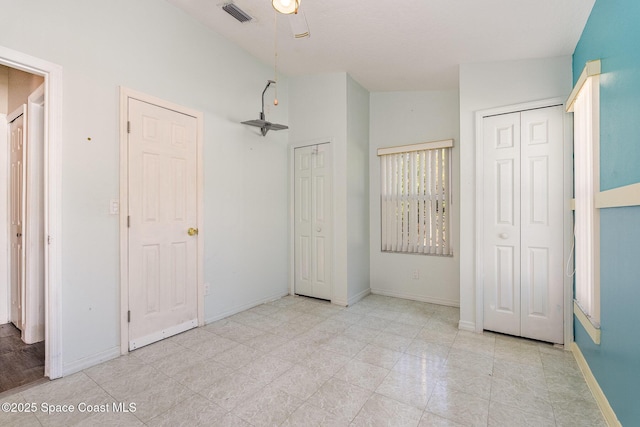 unfurnished bedroom with lofted ceiling, baseboards, visible vents, and multiple closets