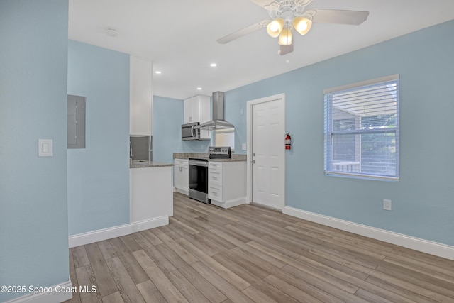 kitchen with stainless steel appliances, baseboards, white cabinets, light wood-type flooring, and wall chimney exhaust hood