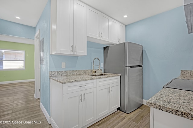 kitchen featuring light stone counters, a sink, white cabinets, light wood-type flooring, and freestanding refrigerator