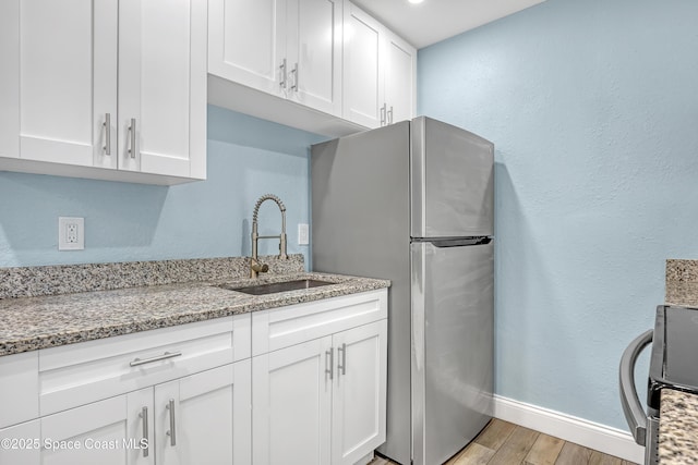 kitchen with light wood-style flooring, appliances with stainless steel finishes, white cabinets, a sink, and baseboards