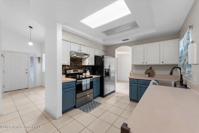 kitchen featuring arched walkways, appliances with stainless steel finishes, blue cabinetry, under cabinet range hood, and a sink