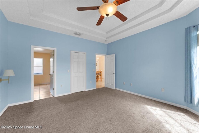 unfurnished bedroom featuring ensuite bathroom, carpet flooring, visible vents, baseboards, and a tray ceiling