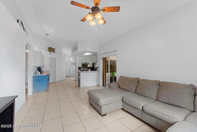 living area with ceiling fan, a textured ceiling, arched walkways, lofted ceiling, and light tile patterned flooring