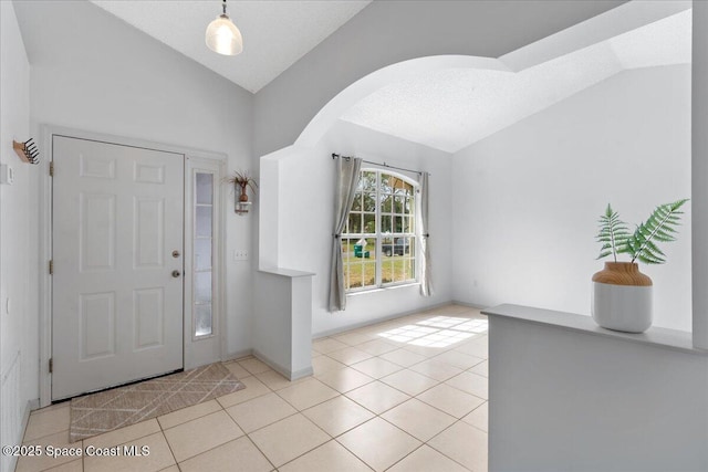 tiled entrance foyer featuring baseboards, arched walkways, and vaulted ceiling