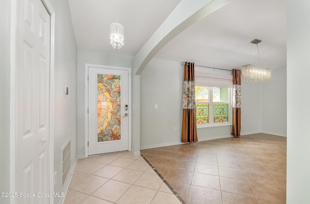 foyer entrance featuring light tile patterned floors, baseboards, arched walkways, and an inviting chandelier