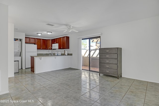 kitchen with ceiling fan, a peninsula, white appliances, stacked washer / dryer, and light stone countertops