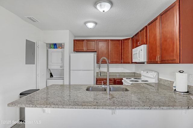 kitchen featuring white appliances, stacked washer and dryer, visible vents, a peninsula, and a sink