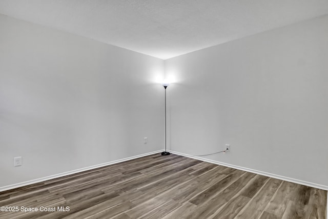 spare room featuring dark wood-type flooring, a textured ceiling, and baseboards