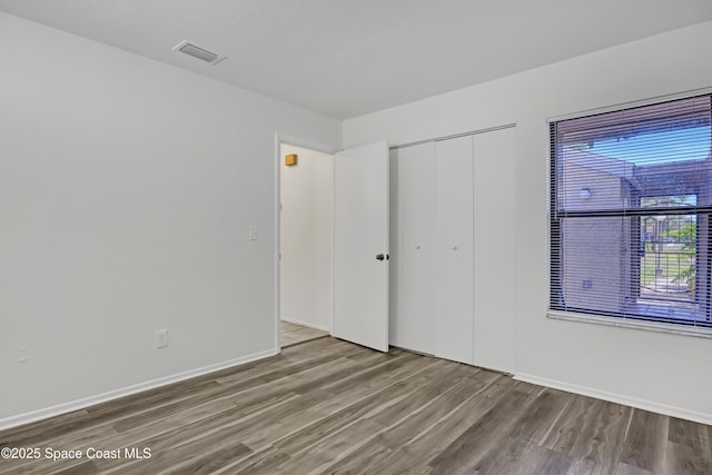 unfurnished bedroom with a closet, wood finished floors, visible vents, and baseboards