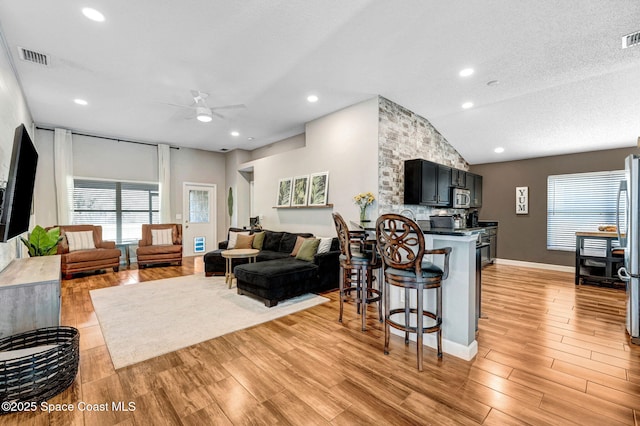 living area with light wood-type flooring, a ceiling fan, vaulted ceiling, and a textured ceiling