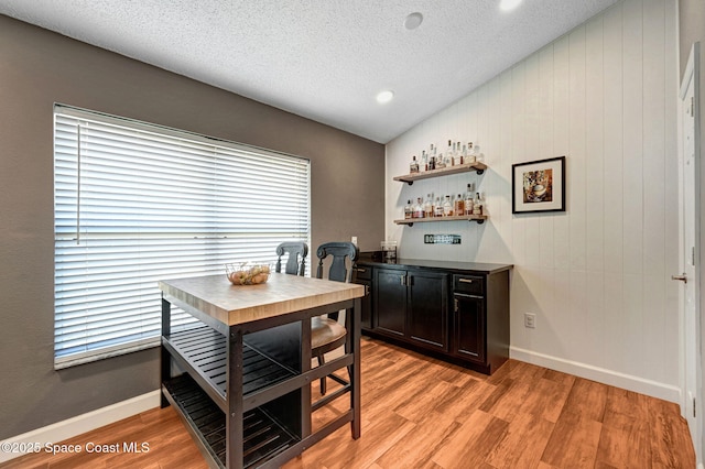 dining area with lofted ceiling, a bar, a textured ceiling, and light wood-style flooring