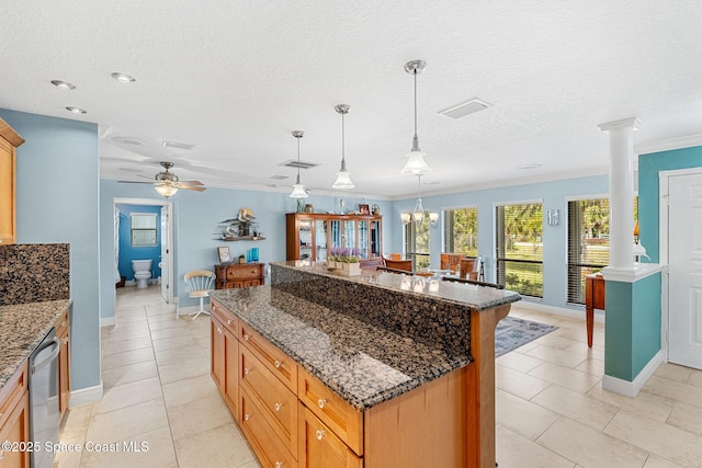 kitchen featuring stainless steel dishwasher, ornamental molding, a center island, and ornate columns