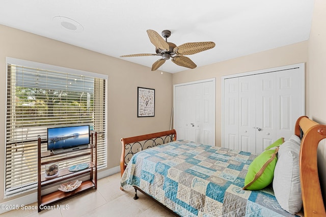 bedroom with tile patterned floors, baseboards, two closets, and ceiling fan