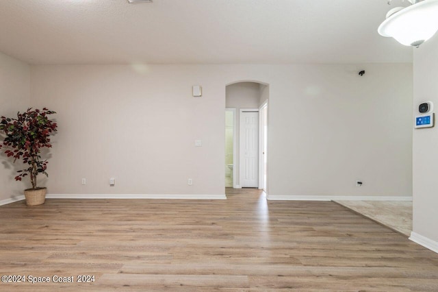 spare room featuring light wood finished floors, baseboards, and arched walkways