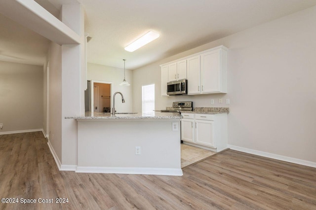 kitchen with light wood finished floors, white cabinets, light stone countertops, stainless steel appliances, and a sink