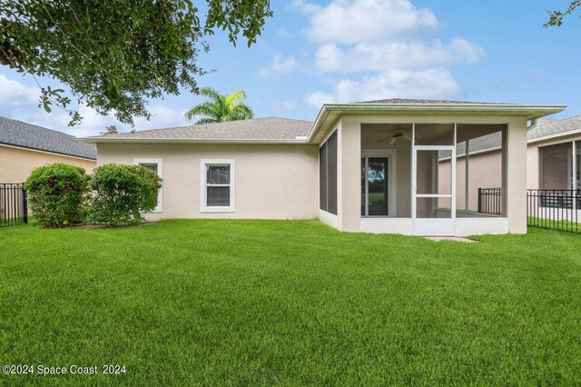 rear view of house with a sunroom, stucco siding, fence, and a lawn