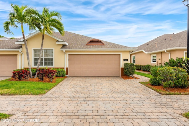 single story home with a shingled roof, decorative driveway, a garage, and stucco siding