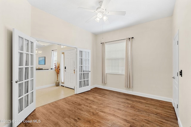 unfurnished room with ceiling fan with notable chandelier, baseboards, and wood finished floors