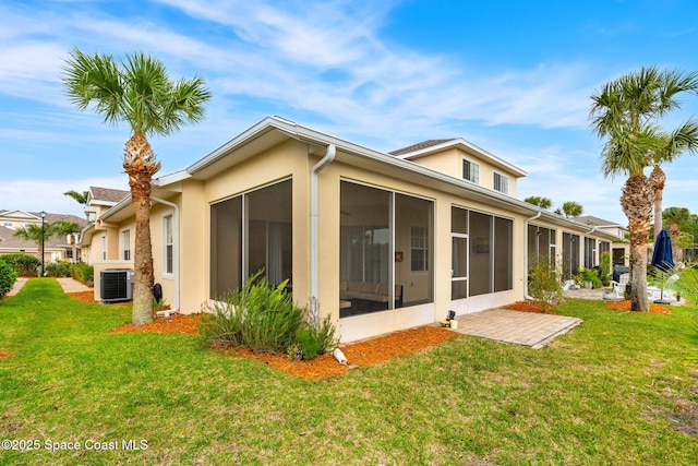 back of property with stucco siding, a lawn, central AC unit, and a sunroom