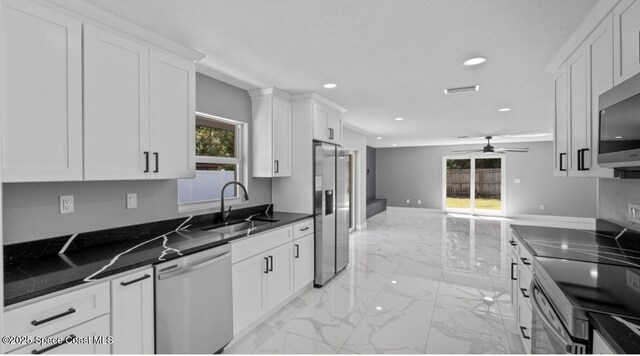 kitchen featuring a sink, stainless steel appliances, white cabinets, dark countertops, and marble finish floor