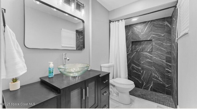 full bath featuring a tile shower, toilet, vanity, and marble finish floor