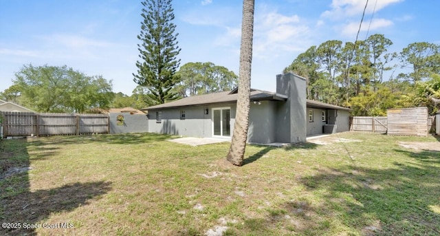 back of property with stucco siding, a gate, a fenced backyard, a yard, and a chimney