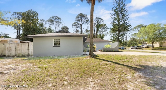 view of property exterior featuring fence, a lawn, and stucco siding