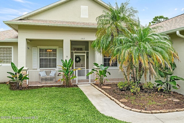 view of exterior entry featuring covered porch, a yard, a shingled roof, and stucco siding