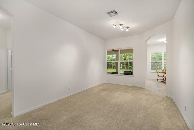 empty room featuring a textured ceiling, arched walkways, light carpet, visible vents, and baseboards