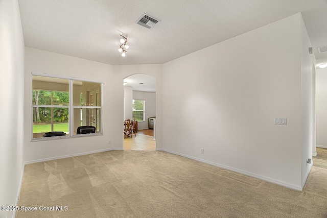 unfurnished room featuring arched walkways, a textured ceiling, light carpet, visible vents, and baseboards