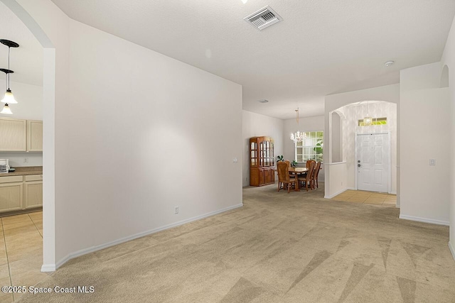 unfurnished room with arched walkways, light colored carpet, visible vents, an inviting chandelier, and baseboards