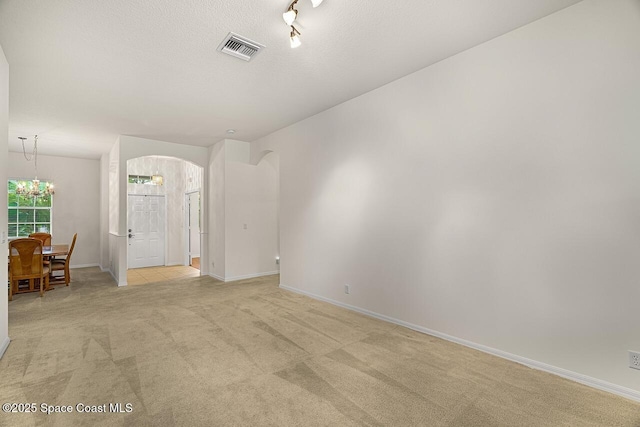 empty room with light carpet, visible vents, arched walkways, an inviting chandelier, and a textured ceiling