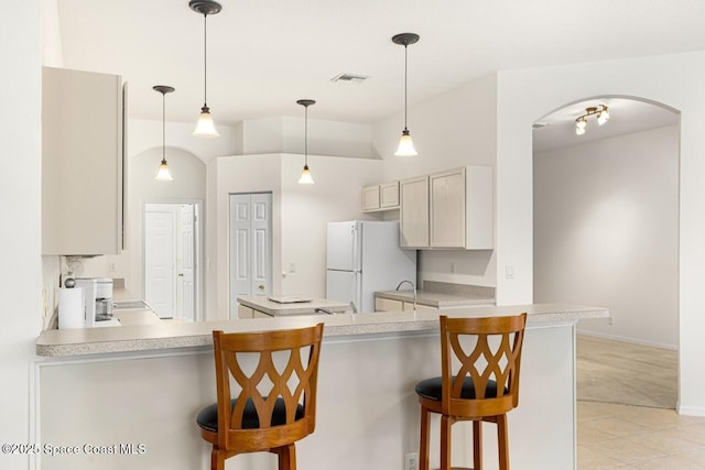 kitchen with arched walkways, visible vents, a breakfast bar area, freestanding refrigerator, and light countertops