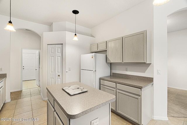 kitchen with arched walkways, gray cabinets, hanging light fixtures, freestanding refrigerator, and a kitchen island