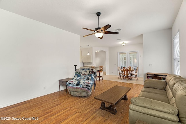 living area with visible vents, arched walkways, baseboards, ceiling fan, and light wood-style floors