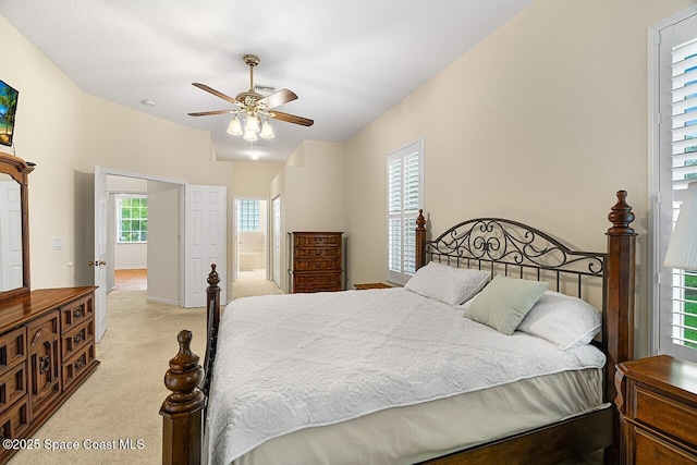 bedroom with baseboards, ensuite bathroom, a ceiling fan, and light colored carpet