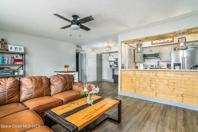 living area featuring a textured ceiling, ceiling fan, dark wood-style flooring, visible vents, and baseboards