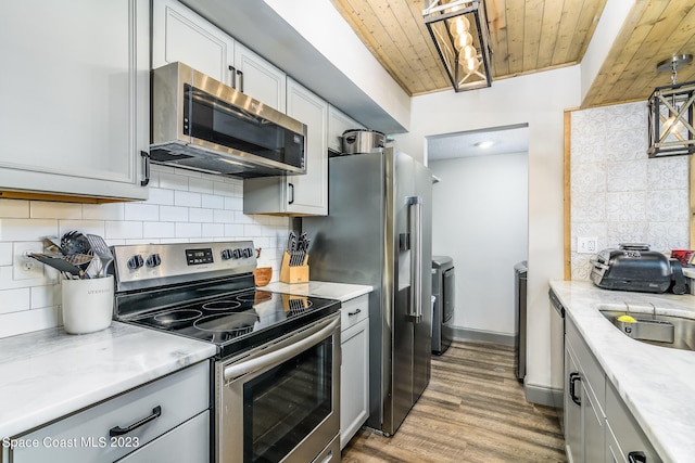 kitchen with wooden ceiling, appliances with stainless steel finishes, wood finished floors, independent washer and dryer, and backsplash