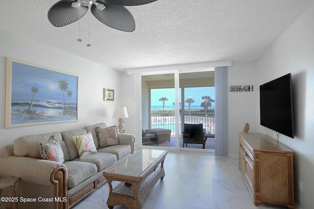 living room featuring a textured ceiling, marble finish floor, a wall of windows, and a ceiling fan