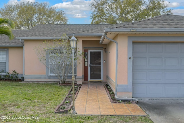 view of exterior entry featuring an attached garage, roof with shingles, a lawn, and stucco siding