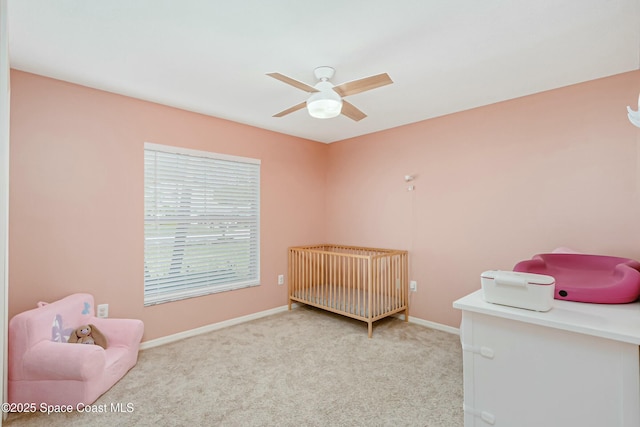 bedroom featuring a ceiling fan, light colored carpet, a crib, and baseboards