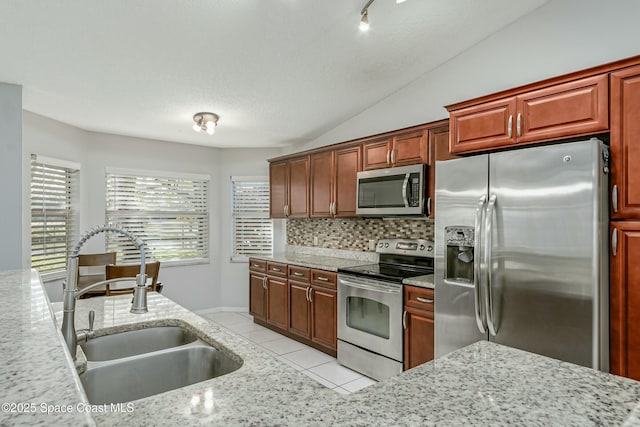 kitchen with light tile patterned floors, decorative backsplash, lofted ceiling, appliances with stainless steel finishes, and a sink