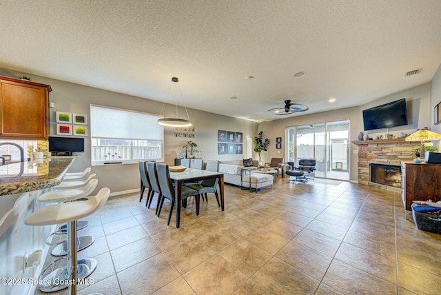 dining space featuring a fireplace, light tile patterned floors, visible vents, a textured ceiling, and baseboards