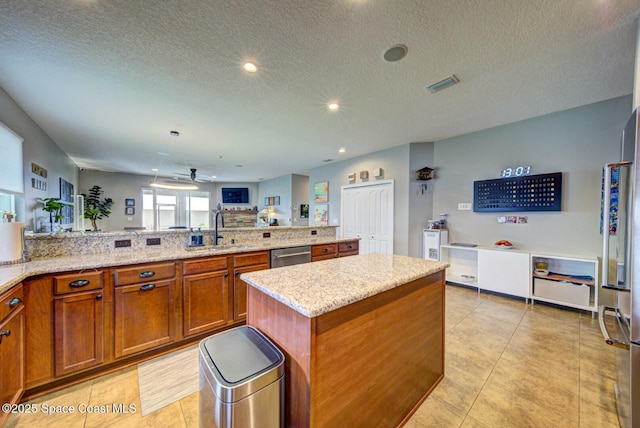 kitchen with a sink, visible vents, appliances with stainless steel finishes, brown cabinets, and light stone countertops